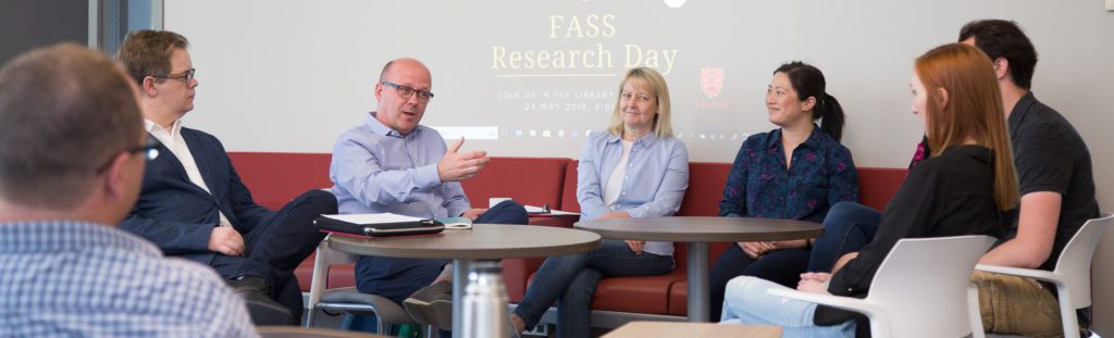 Huron faculty members sit around a table in the library, discussing research during FASS Day 2018.