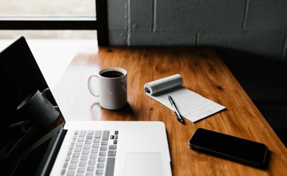 A computer, a mug, a notepad, and a pencil case are arranged on a desk.