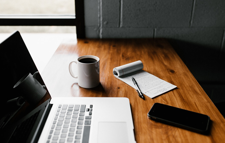 A photo of a computer with a mug and notebook nearby.