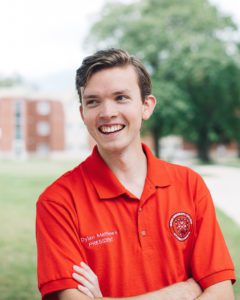 Past CURL Fellow and HUCSC Dylan Matthews smiles on campus, wearing a Huron-branded collared shirt.