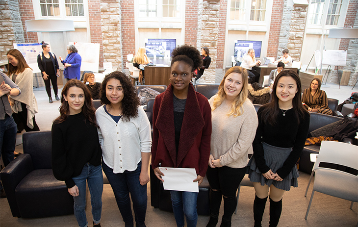 A photo of the 2019-20 school year CURL Fellowship winners at the 2019 Fall Exhibition. They are smiling in the Huron Commons, and behind them is a row of student research posters.