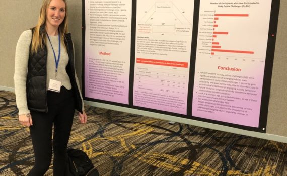 CURL Travel Bursary winner Shannon Ward smiles next to her poster at the SSEA conference in Toronto, Ontario. Her poster is entitled "Challenge Accepted: Exploring Predictors of Risky Online Behaviours in Emerging Adults." Shannon has long, blonde hair and wears a tan sweater and black leggings.