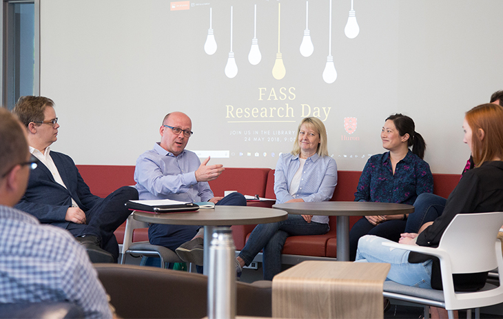 A group of Huron professors chat around a table in the Huron Library Commons.