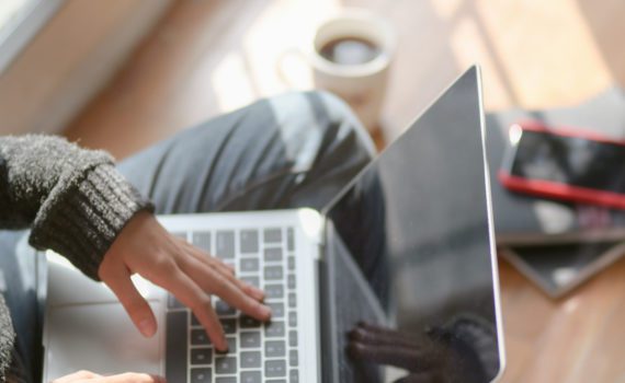 A view from above of a person sitting on the floor and typing on their laptop. They are dressed in cozy clothes.
