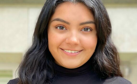 A smiling photo of Ivania Salmeron. She is a Huron student with long, dark hair. She is wearing a black turtleneck.