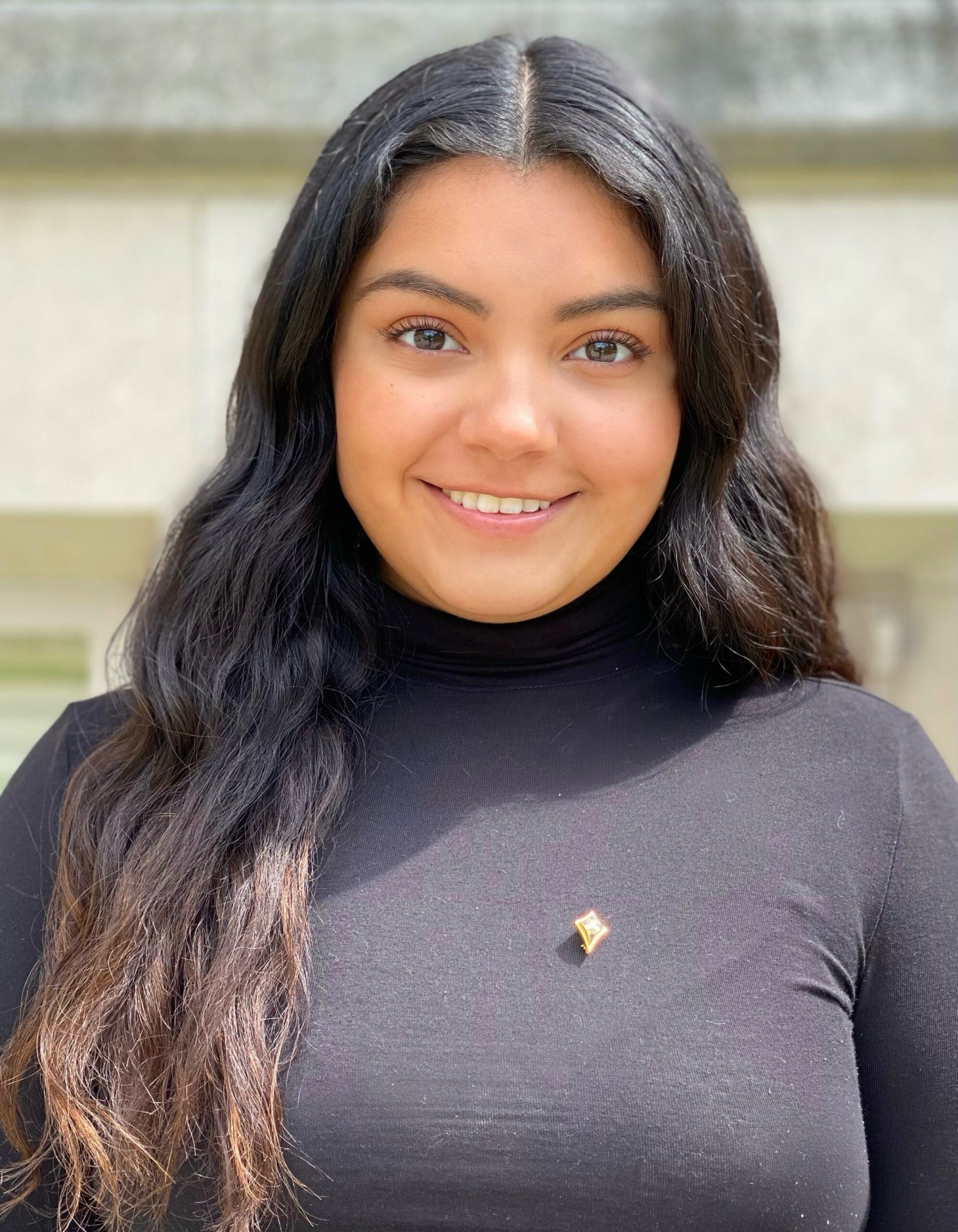 A smiling photo of Ivania Salmeron. She is a Huron student with long, dark hair. She is wearing a black turtleneck.