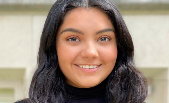 A smiling photo of Ivania Salmeron. She is a Huron student with long, dark hair. She is wearing a black turtleneck.