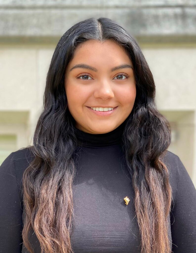 A smiling photo of Ivania Salmeron. She is a Huron student with long, dark hair. She is wearing a black turtleneck.