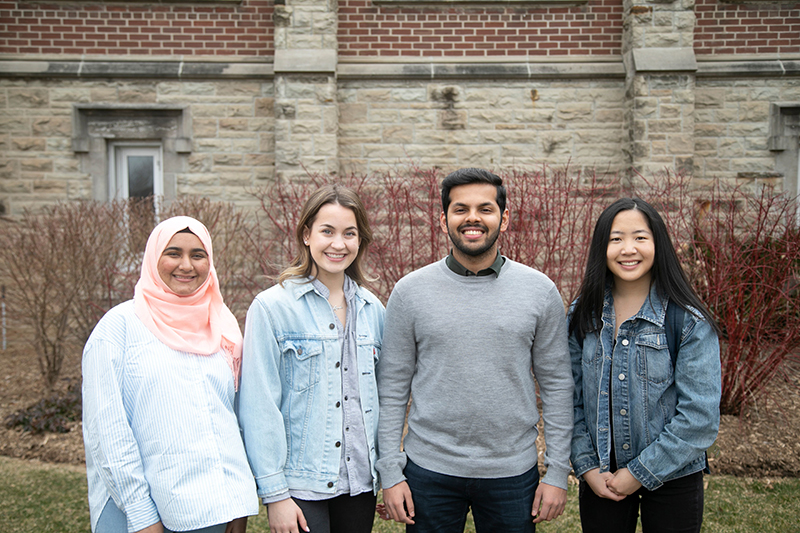 Four different students stand in a row outside Huron University College, smiling.