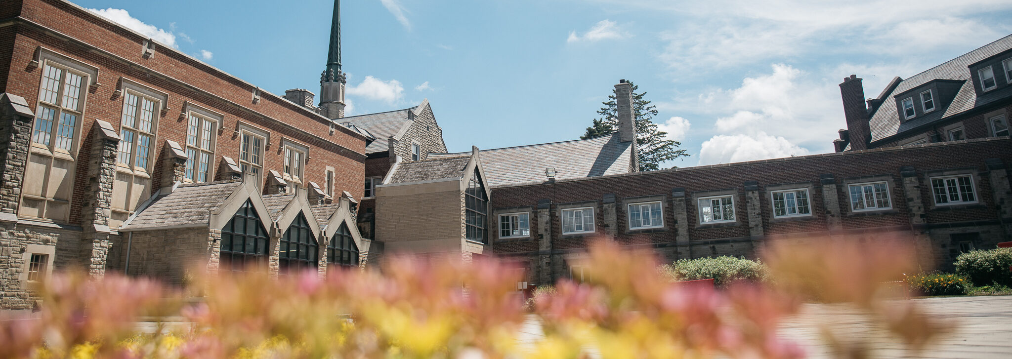 A photograph of Huron University College at daytime in the spring. A field of blurry flowers line the bottom of the foreground.