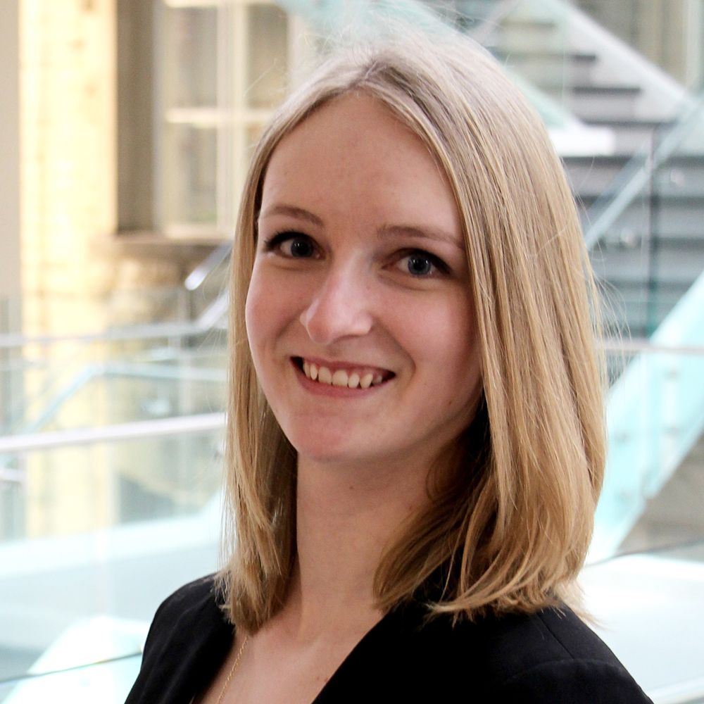 A smiling photo of Alex Ryken. She has a blonde lob haircut and a light complexion, and she's wearing a fancy blazer.