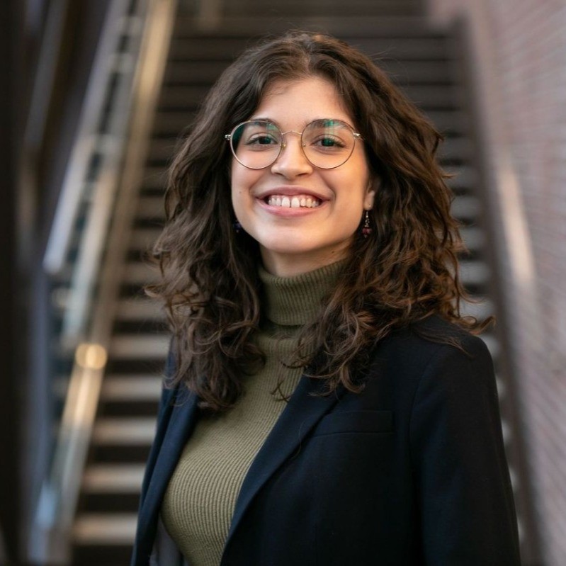 Ana_headshot A headshot of Ana Miranda Guimaraes. She has a bright, friendly smile and round, gold glasses. She is wearing a green turtleneck and a black blazer, and she has shoulder-length, voluminous, wavy hair.