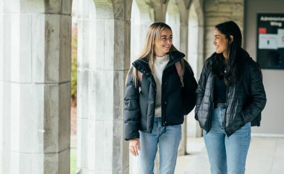 Two students walking outside on the Huron campus. They both have long hair and jackets.